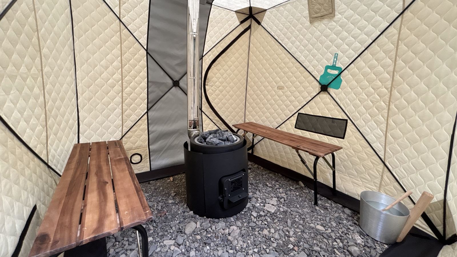 テント内部。木のベンチと薪ストーブ、サウナストーン